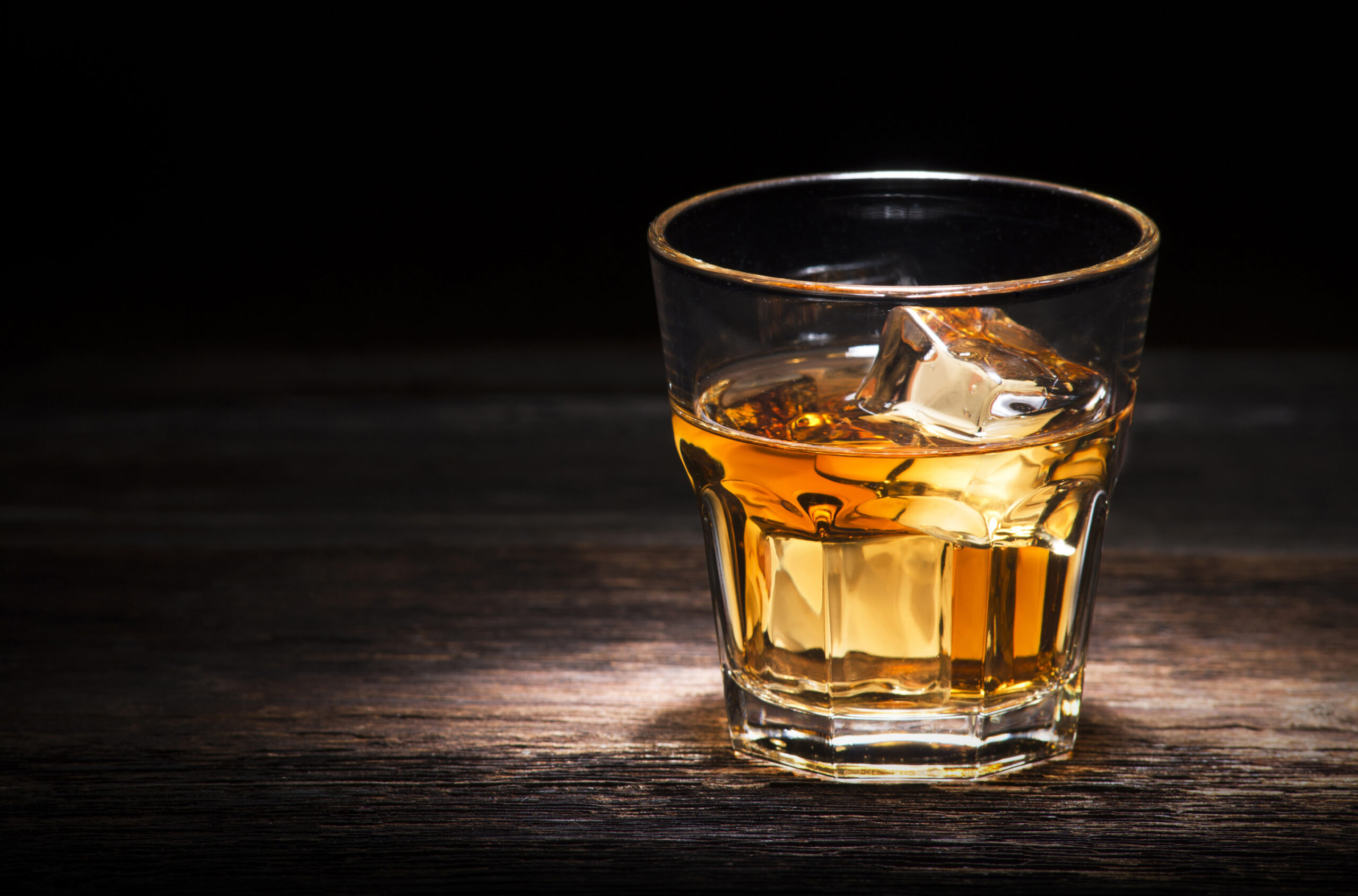 Glass of whiskey on wooden background close up